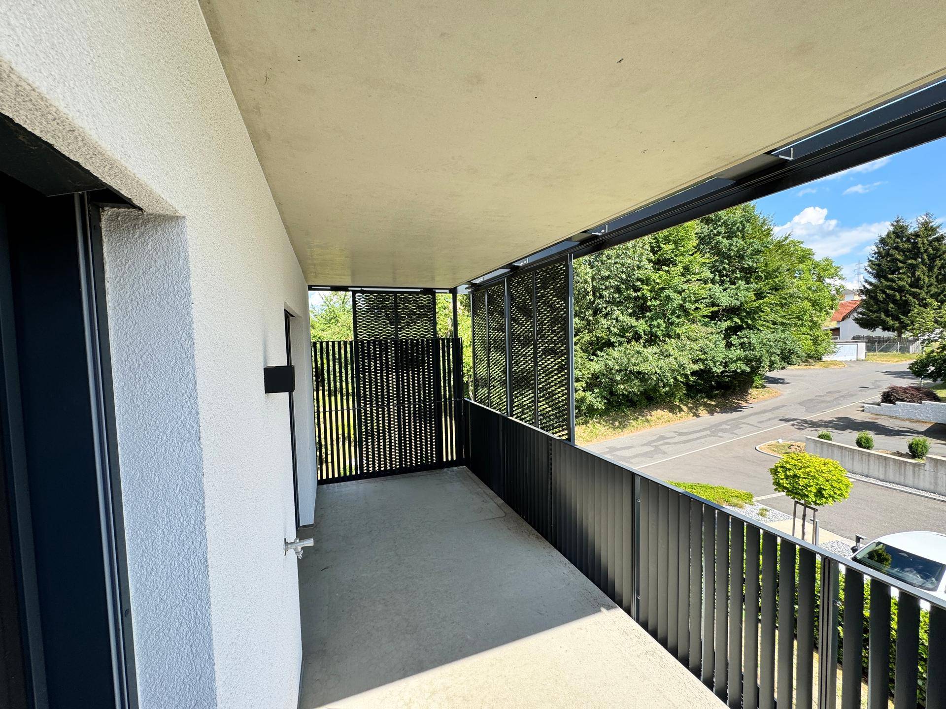 Langer Balkon mit modernem schwarzen Geländer und Blick auf die grüne Umgebung und die Straße.