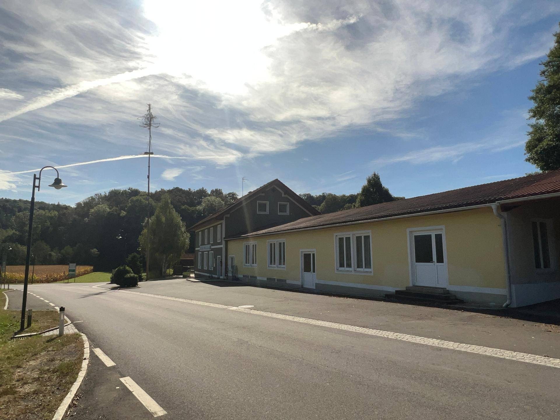 Seitenansicht des Gebäudes mit angrenzendem Anbau, Straße und ländlicher Umgebung unter hellem Himmel.