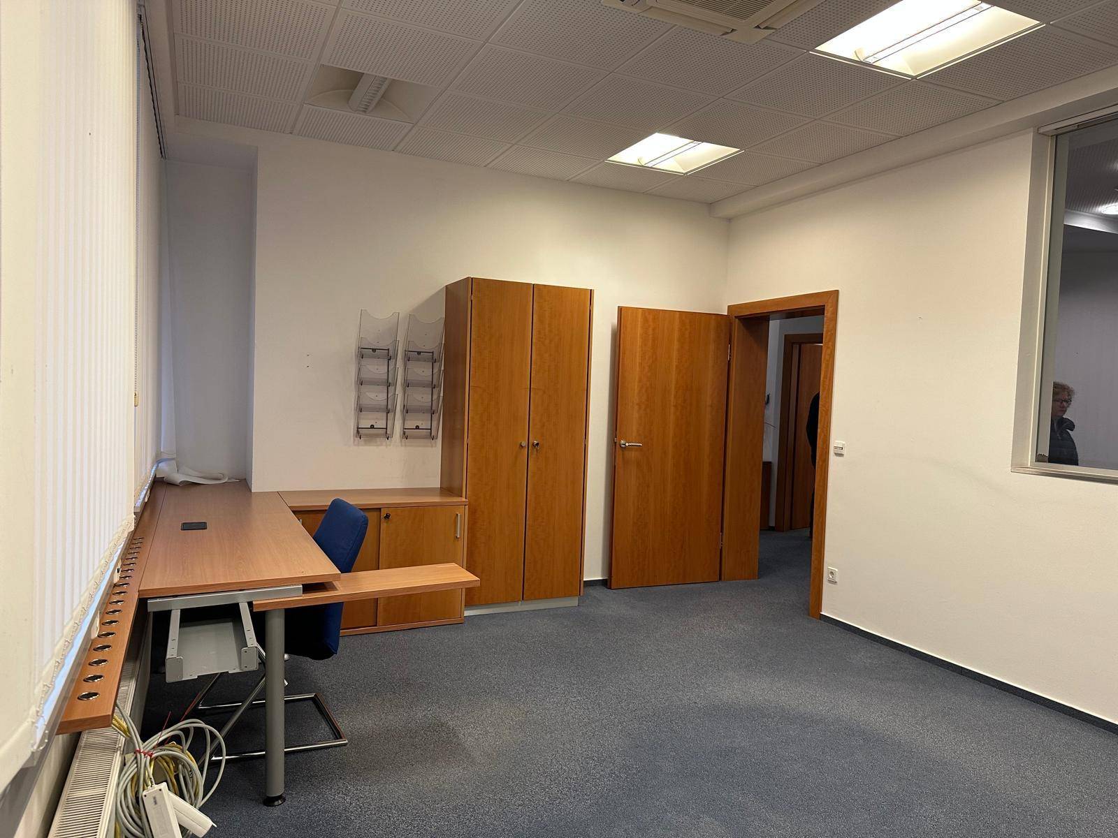 Geräumiges Büro mit Teppichboden, Schreibtisch und Einbauschränken, gut beleuchtet.