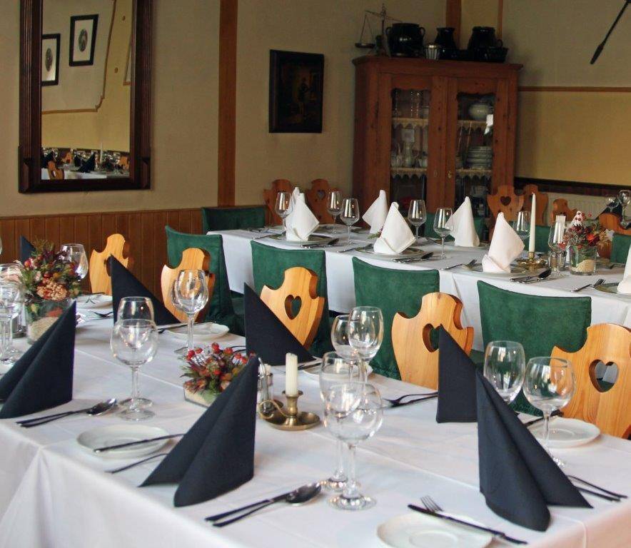 Festlich gedeckter Esstisch mit weißen Tischdecken, grünen Stuhlhussen und traditionellen Holzstühlen.