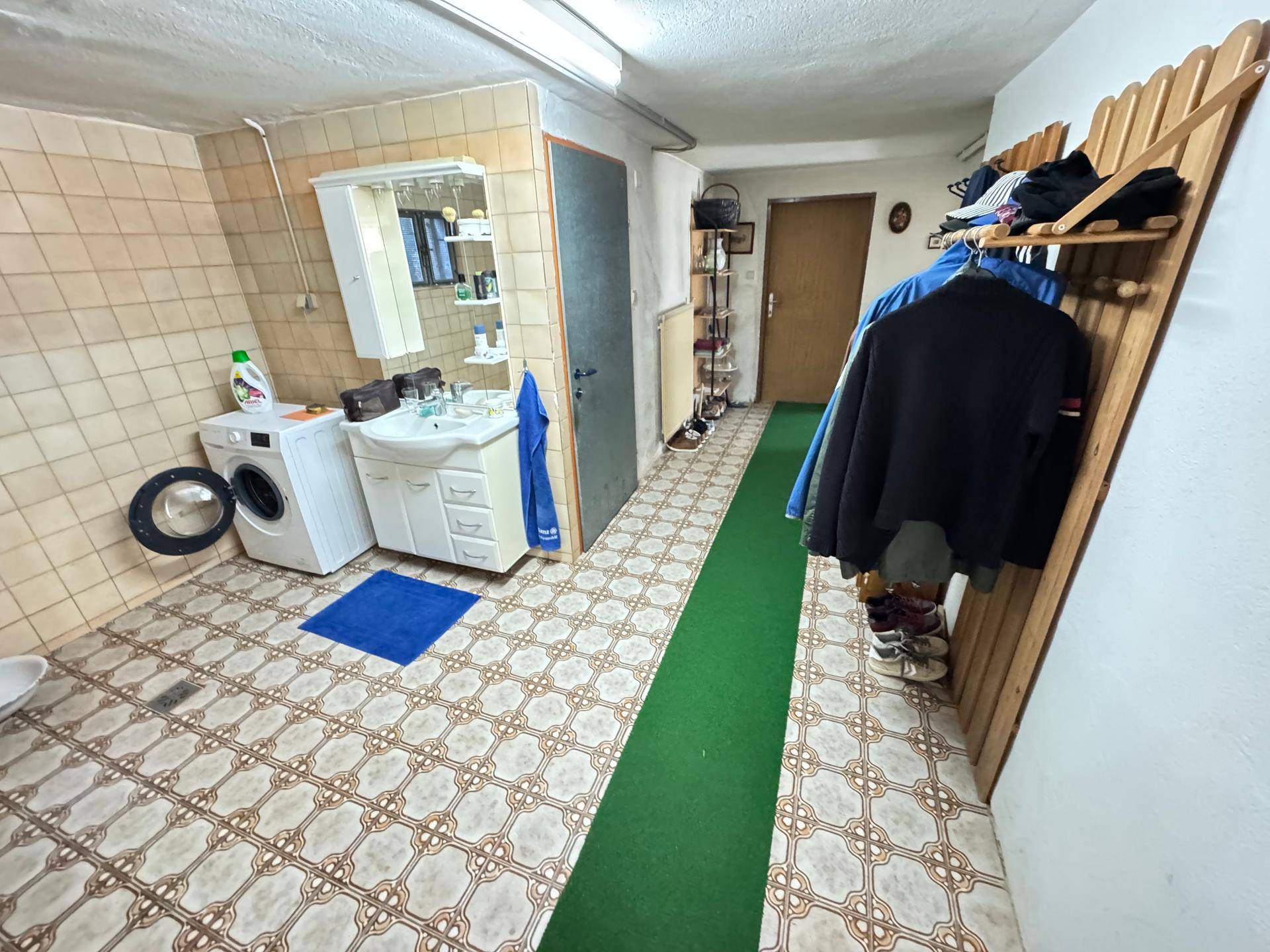 Waschküche im Keller mit Waschmaschine, Waschbecken und gemusterten Fliesen, auch als Garderobe genutzt.