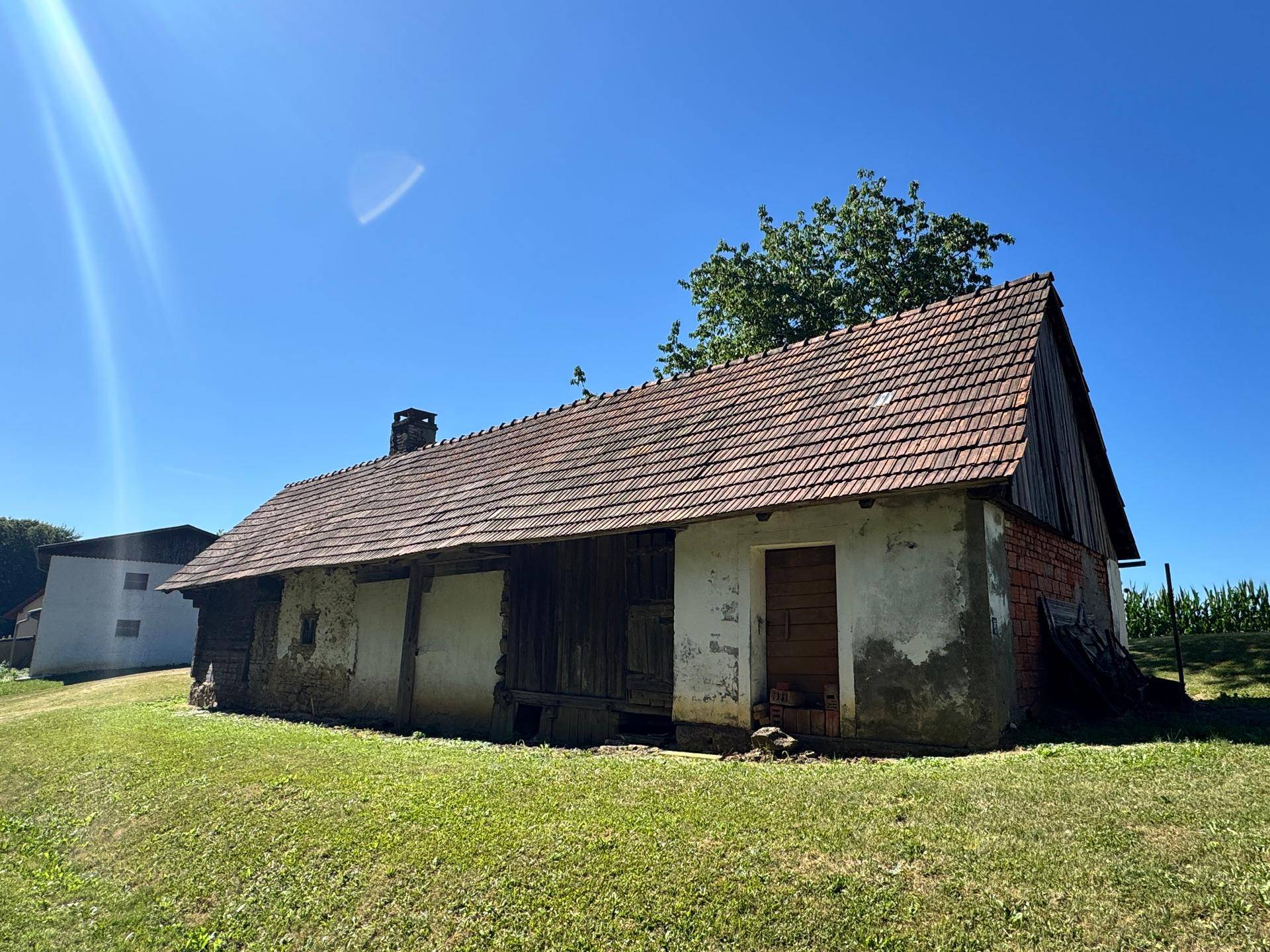 Rustikales Gebäude mit verwitterter Fassade und Ziegeldach, umgeben von Grünflächen.