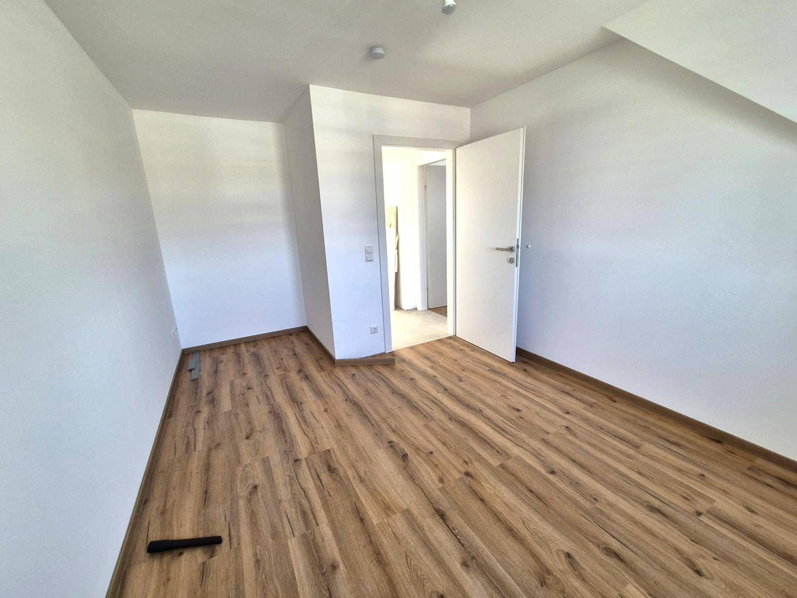 Leeres Zimmer mit Laminatboden und weiß gestrichenen Wänden, bereit zum Einzug.