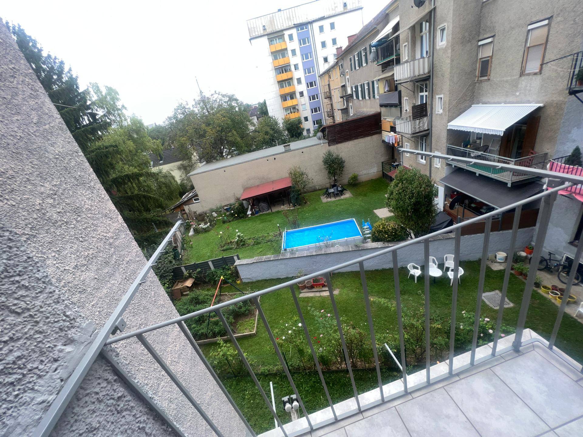Balkon mit Blick auf einen gepflegten Gemeinschaftsgarten mit Pool und Spielgeräten.