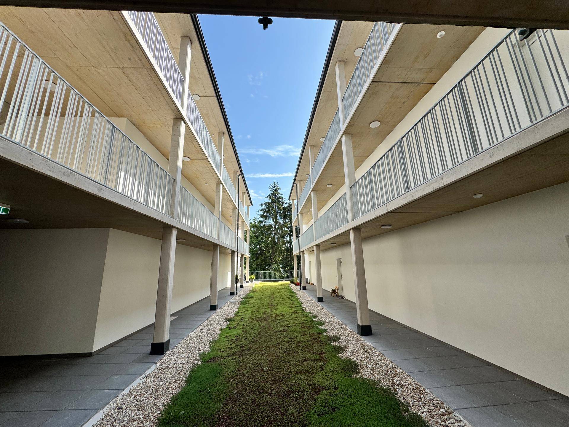 Symmetrischer Blick durch den begrünten Innenhof zwischen zwei Gebäudeflügeln mit Balkonen.