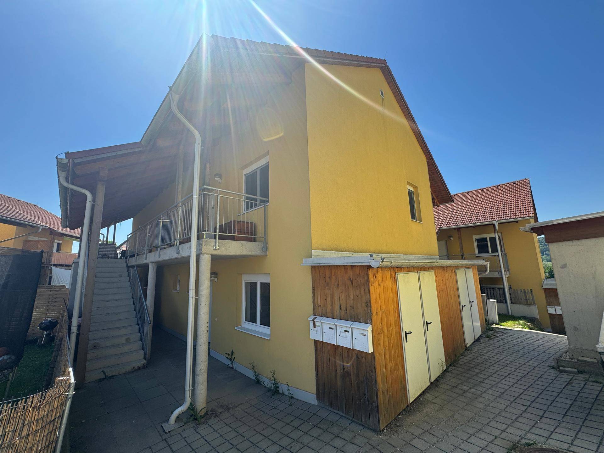 Gelbes Mehrfamilienhaus mit mehreren Balkonen und Außentreppe unter blauem Himmel.