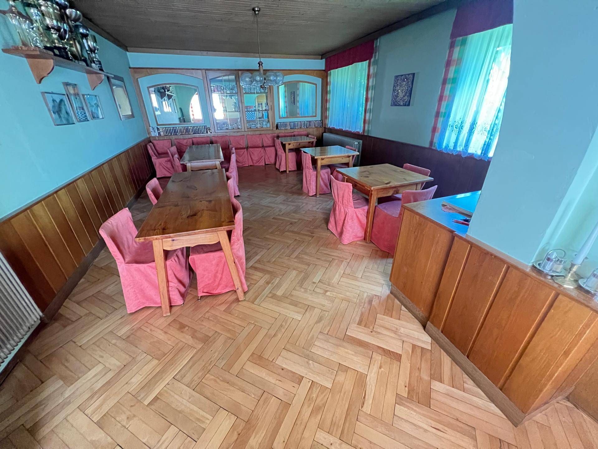 Geräumiger Essbereich mit Holztischen, rosa Stuhlhussen und Fischgrätparkett.