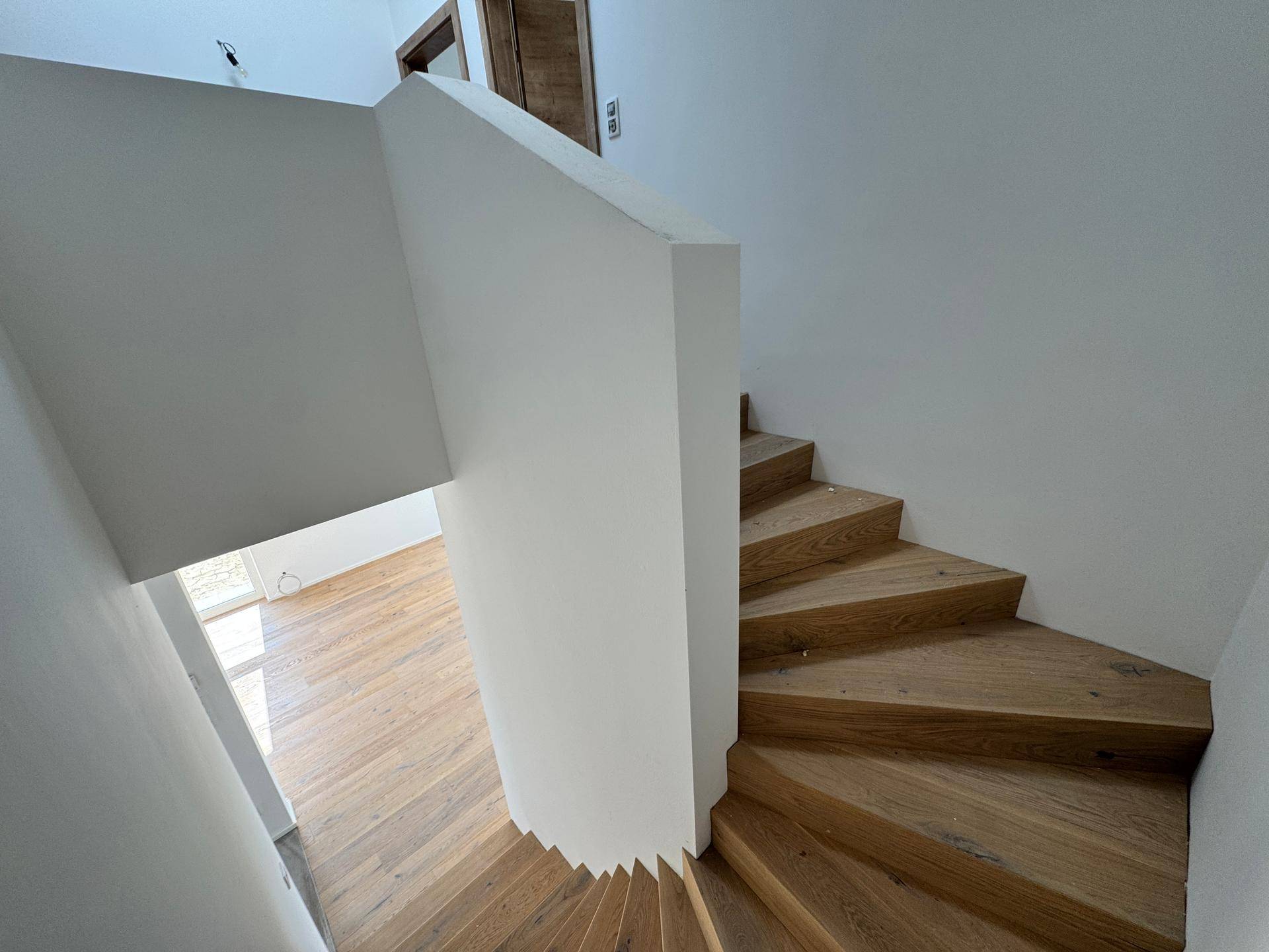 Elegante Holztreppe mit weißem Geländer, die sich spiralförmig nach unten windet.