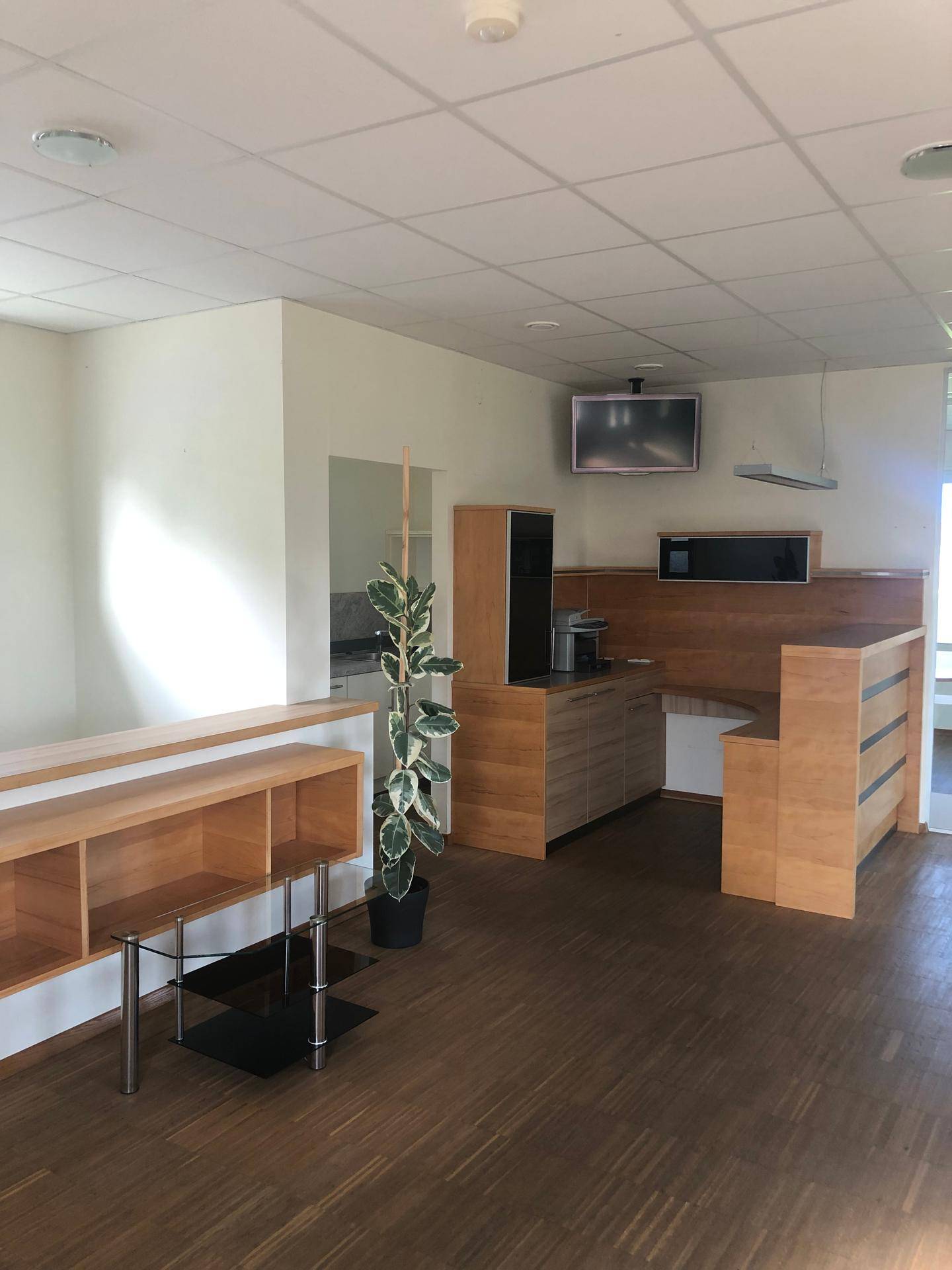 Offener Empfangsbereich oder Büro mit Holzelementen, Regalen und einer Kaffeemaschine.