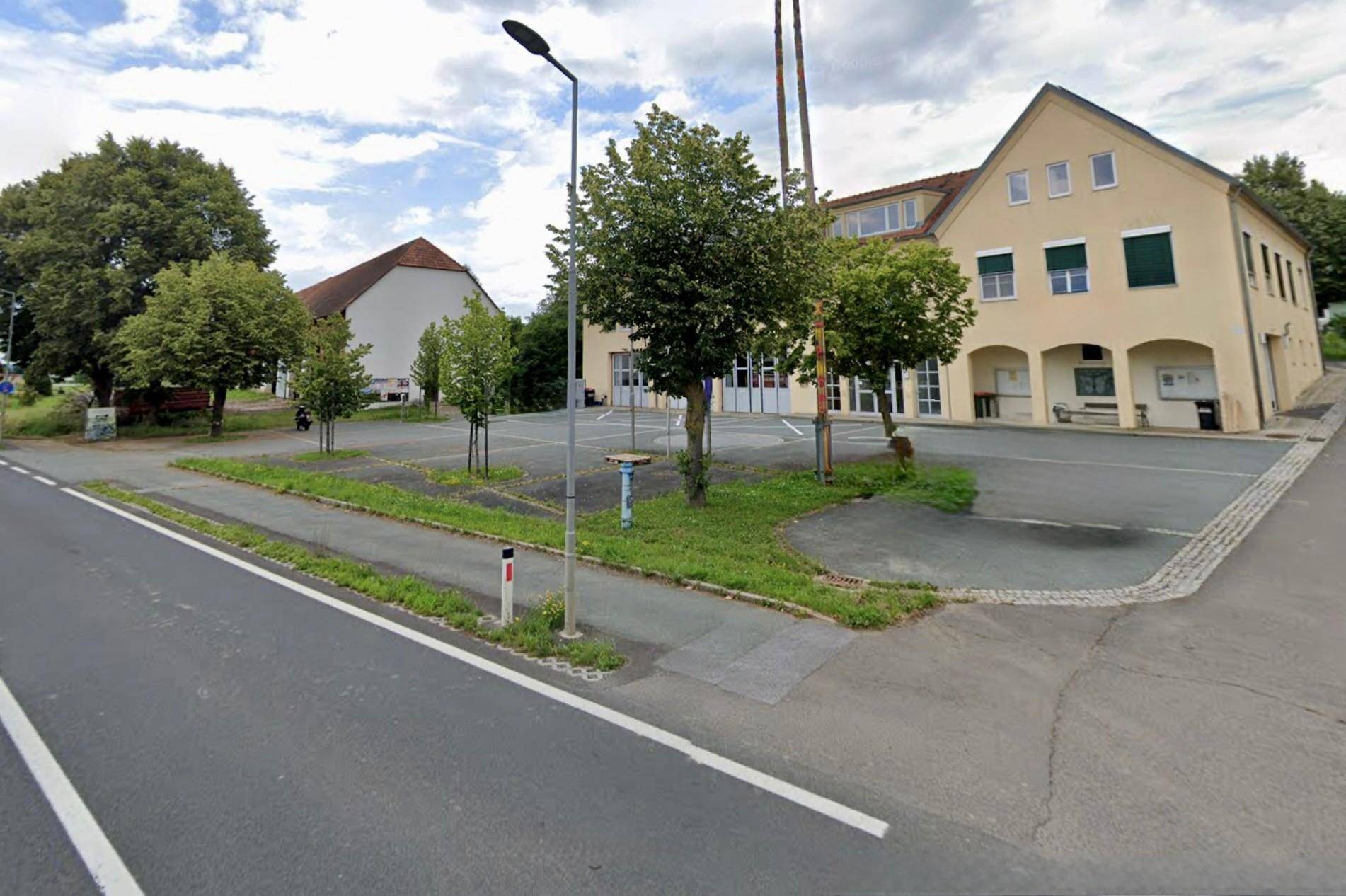Gebäudeansicht mit Parkplätzen, Bäumen und Straße an einem bewölkten Tag.
