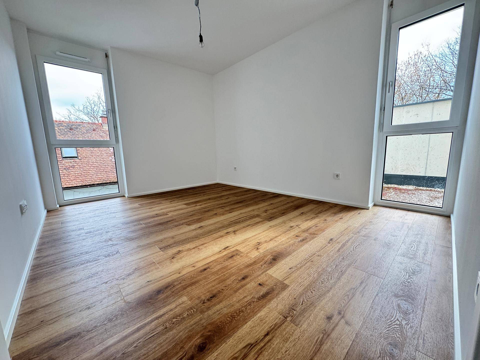 Geräumiges Schlafzimmer mit zwei großen Fenstern und Holzboden, ideal für viel Tageslicht.