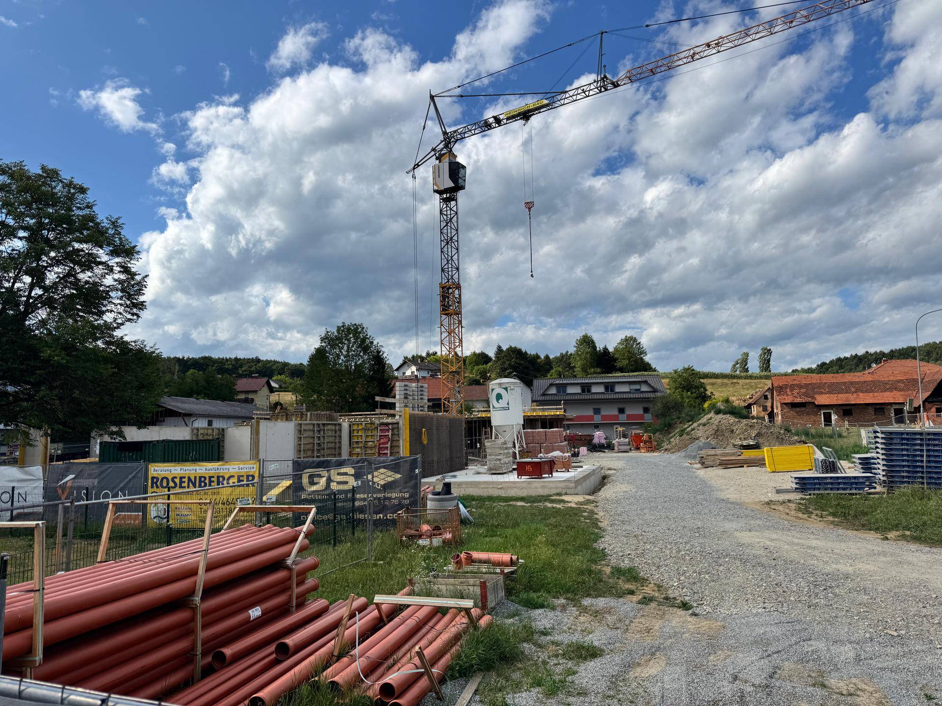 Übersicht der Baustelle mit Kran, Rohren und weiteren Baumaterialien in ländlicher Umgebung.