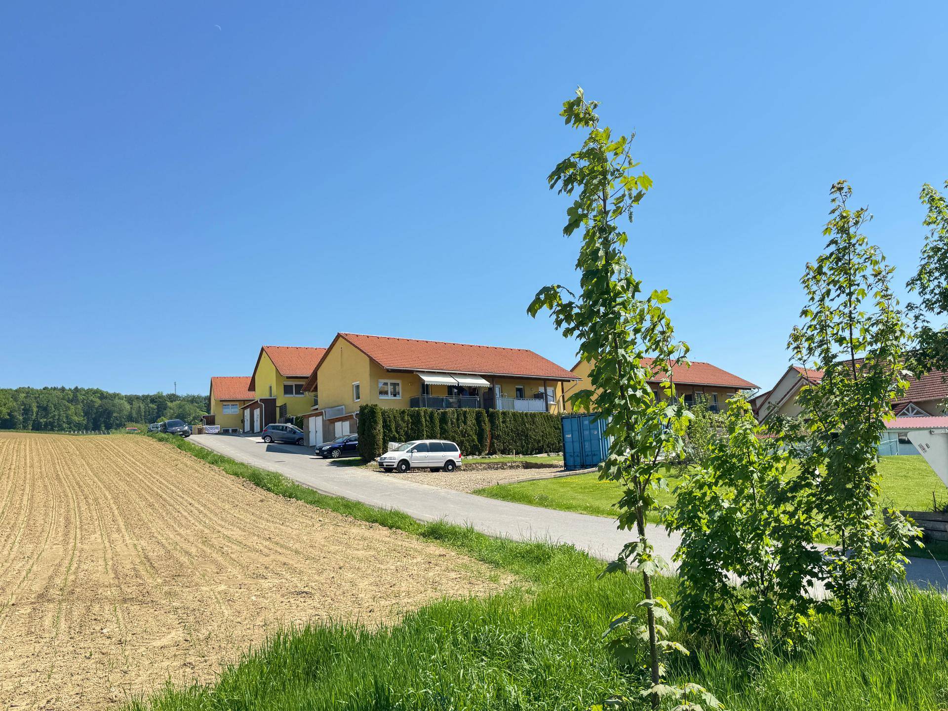 Wohnsiedlung mit gelben Häusern und Feldern in ländlicher Umgebung unter blauem Himmel.