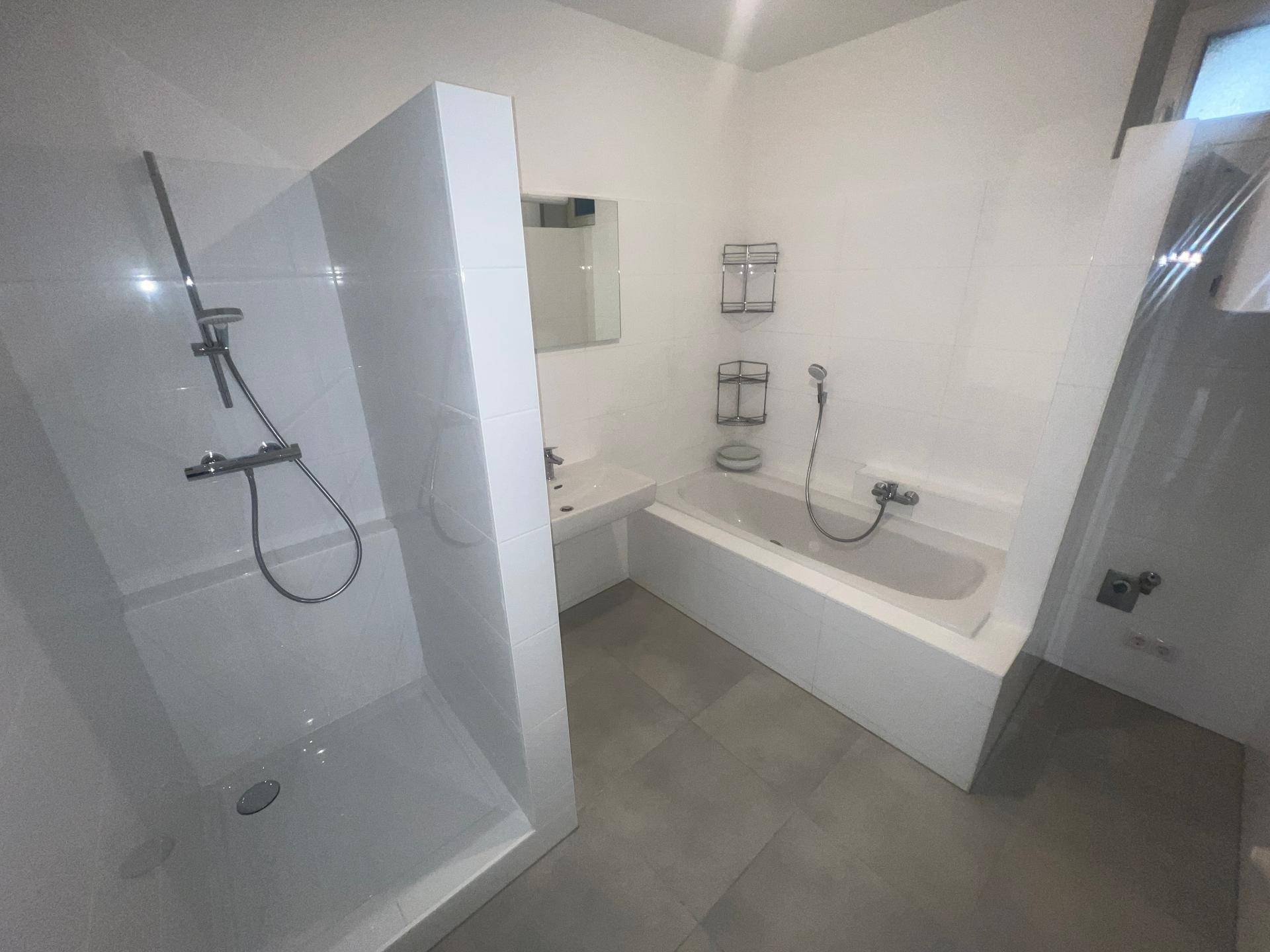 Modernes Badezimmer mit Badewanne, Dusche, Waschbecken und grauen Bodenfliesen.