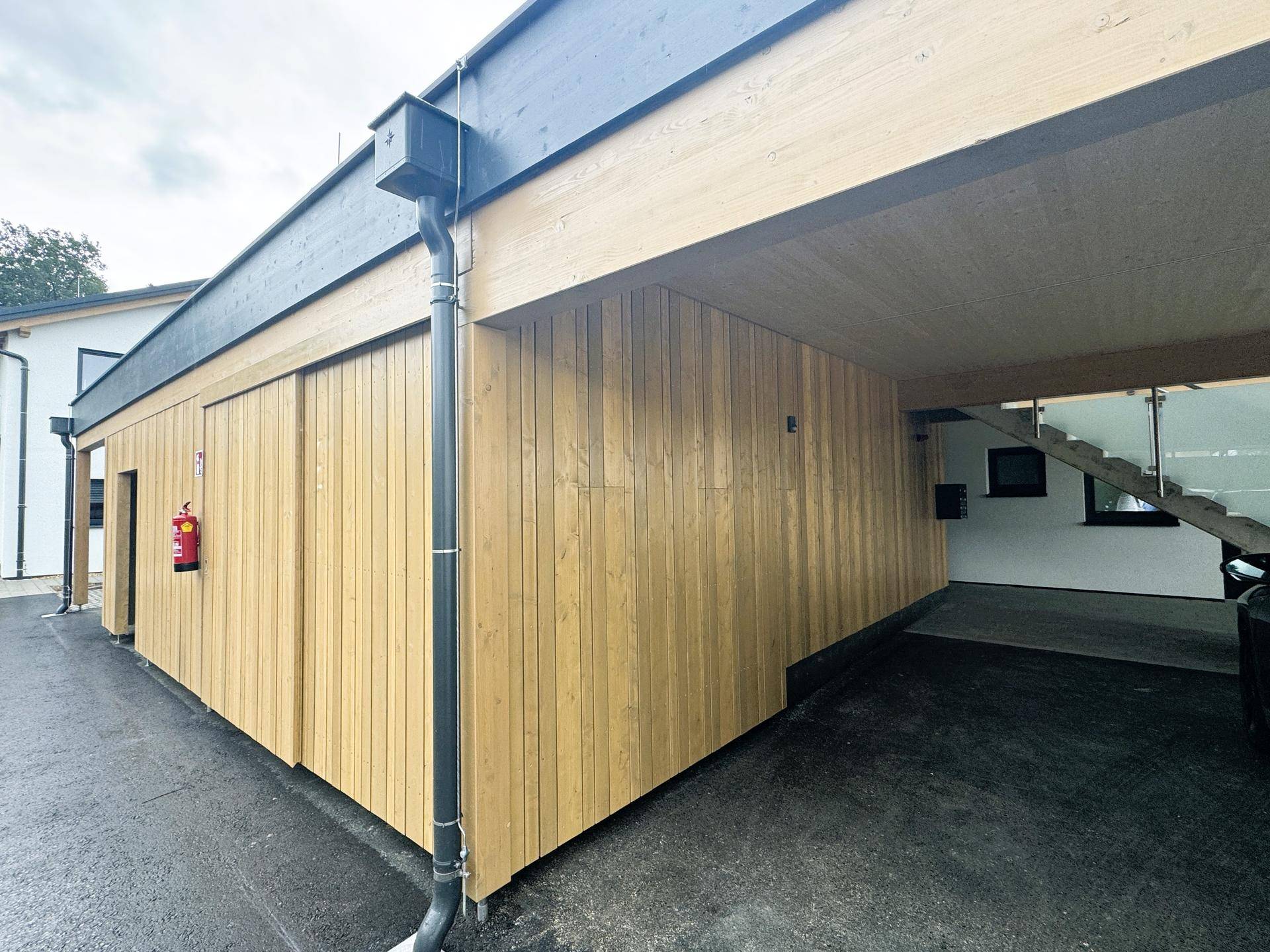 Moderner Carport und Abstellraum mit Holzverkleidung und Zugang zum Gebäude.