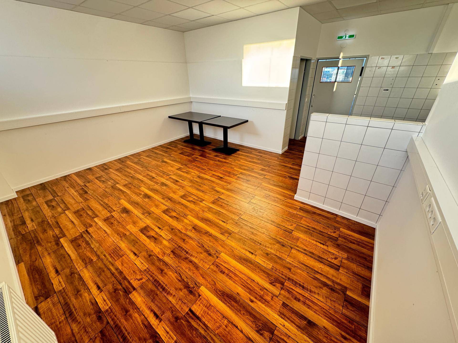 Heller Raum mit Holzboden und weißen Wänden, ausgestattet mit einem Tisch und Blick auf einen Flur.
