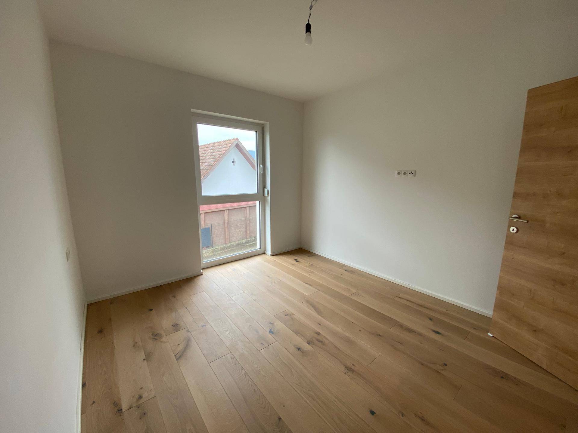 Helles Schlafzimmer mit Holzboden und Fenster mit Zugang zu einem französischen Balkon.