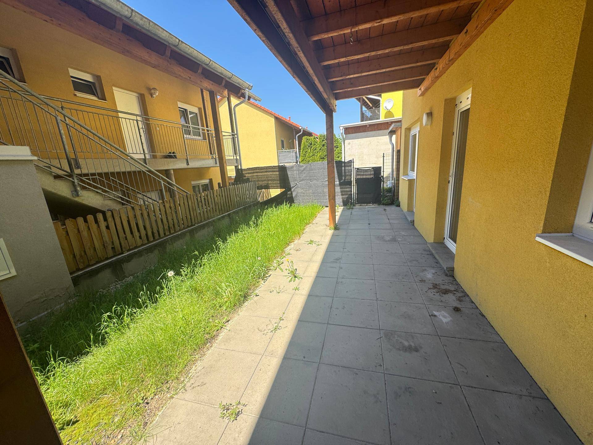 Überdachte Terrasse mit gepflastertem Boden und angrenzender Grünfläche.