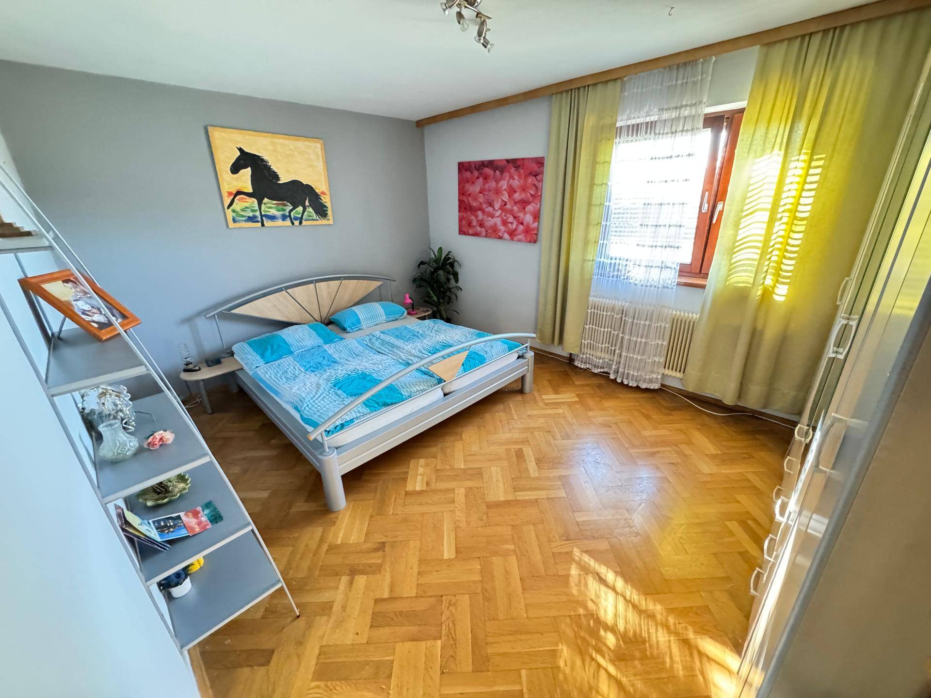 Schlafzimmer mit Parkettboden, modernem Bett und farbenfrohen Bildern an der Wand.