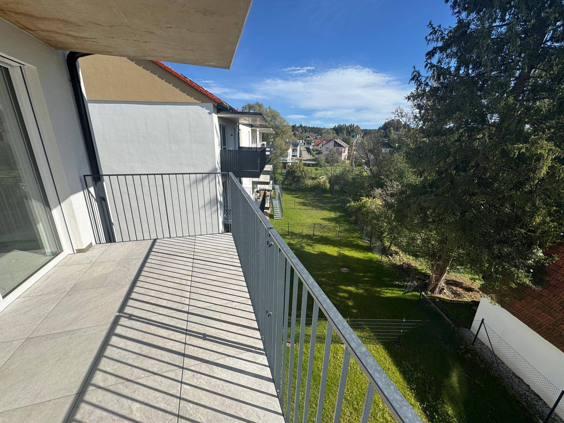 Geräumiger Balkon mit Fliesenboden und Blick auf eine grüne Umgebung und weitere Gebäude.
