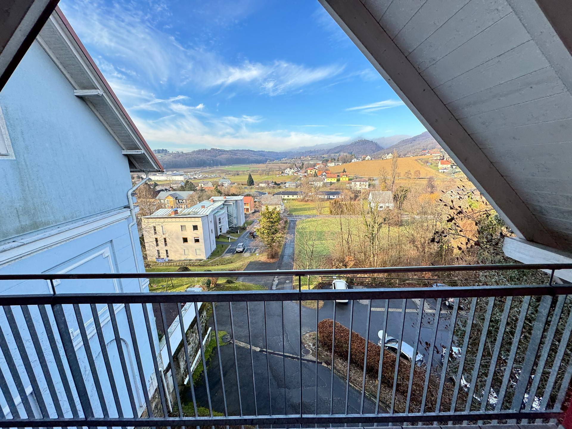 Balkon mit Blick auf die umliegende Wohngegend und grüne Hügel unter blauem Himmel.
