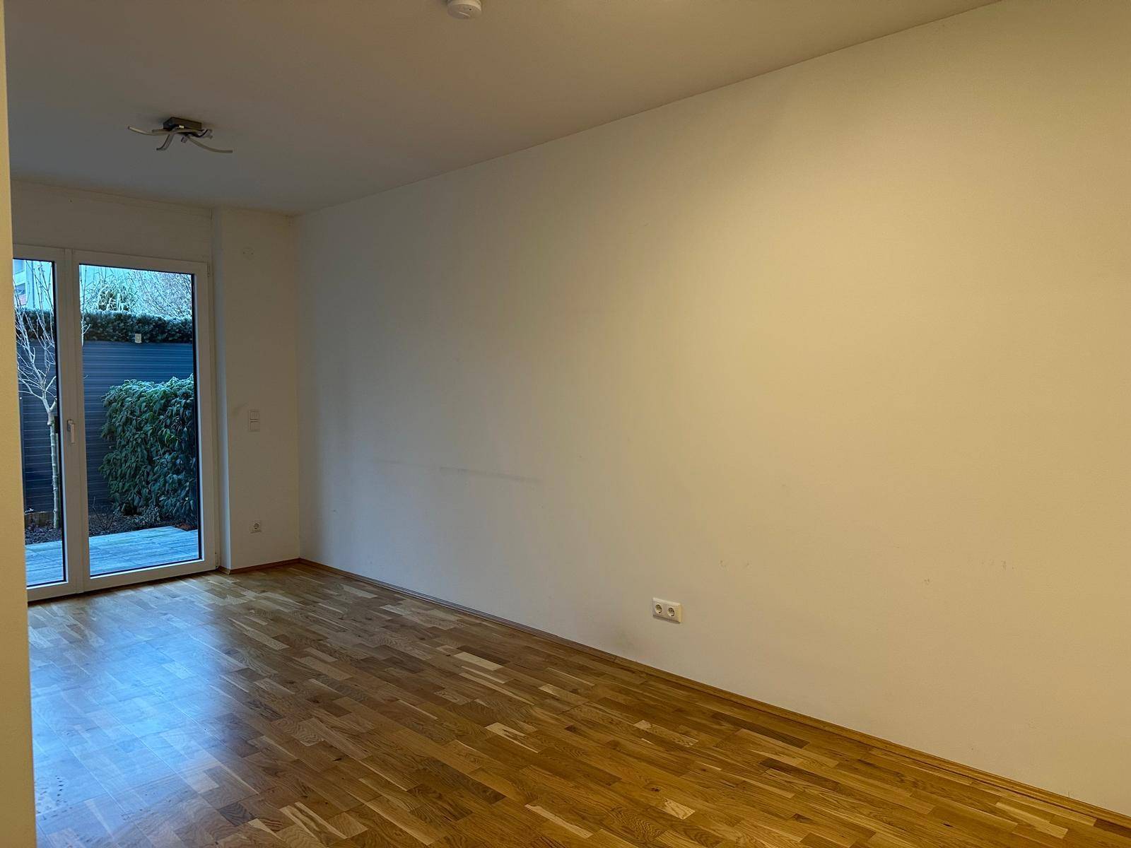 Geräumiger Wohnbereich mit hellem Holzboden und großen Fenstern zum Garten.