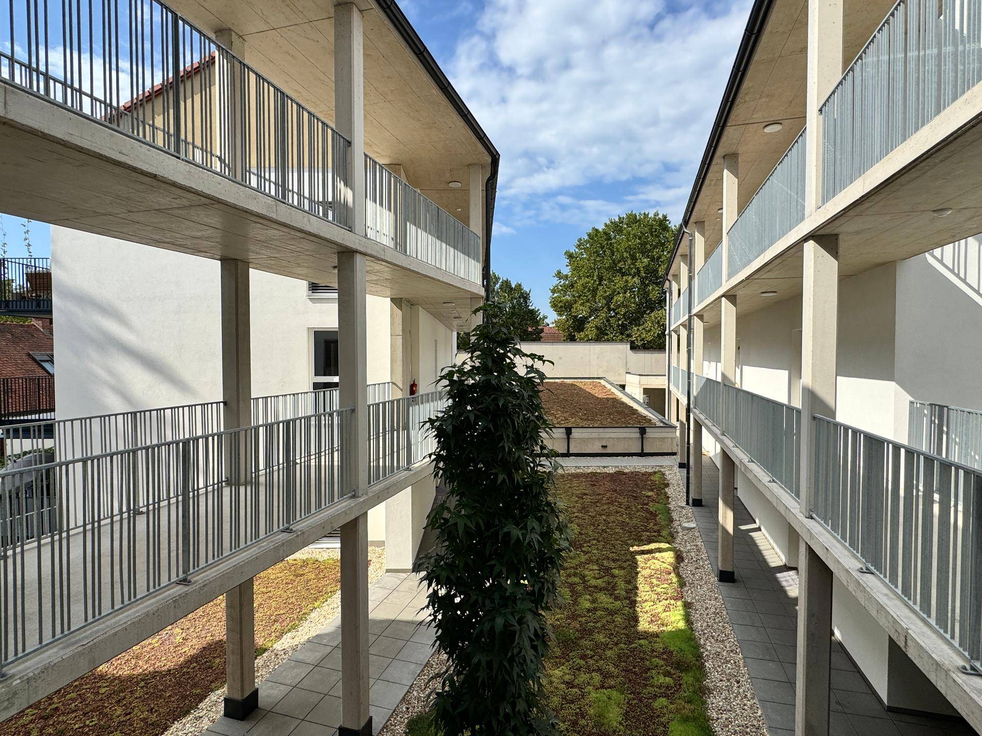 Blick von oben auf den begrünten Innenhof zwischen den modernen Wohngebäuden unter blauem Himmel.