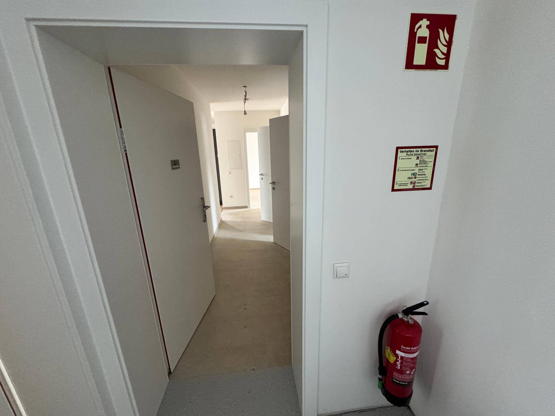 Eingangsbereich mit Feuerlöscher und Hinweisschildern, der zu den Wohnungen führt.