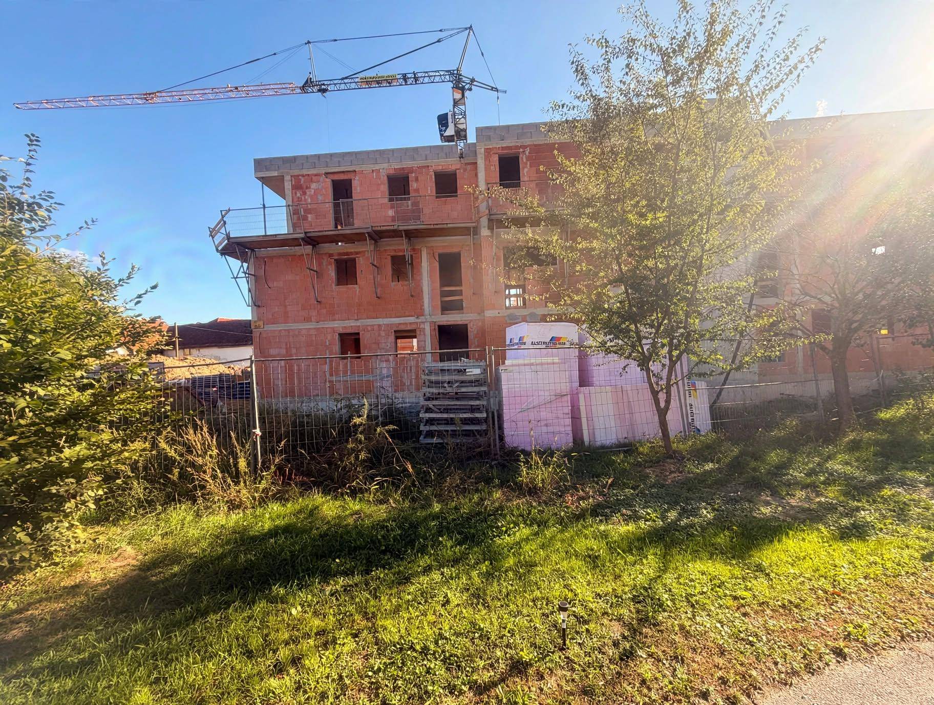 Baustelle mit einem Rohbau, Kran und Isoliermaterialien unter strahlendem Sonnenschein.