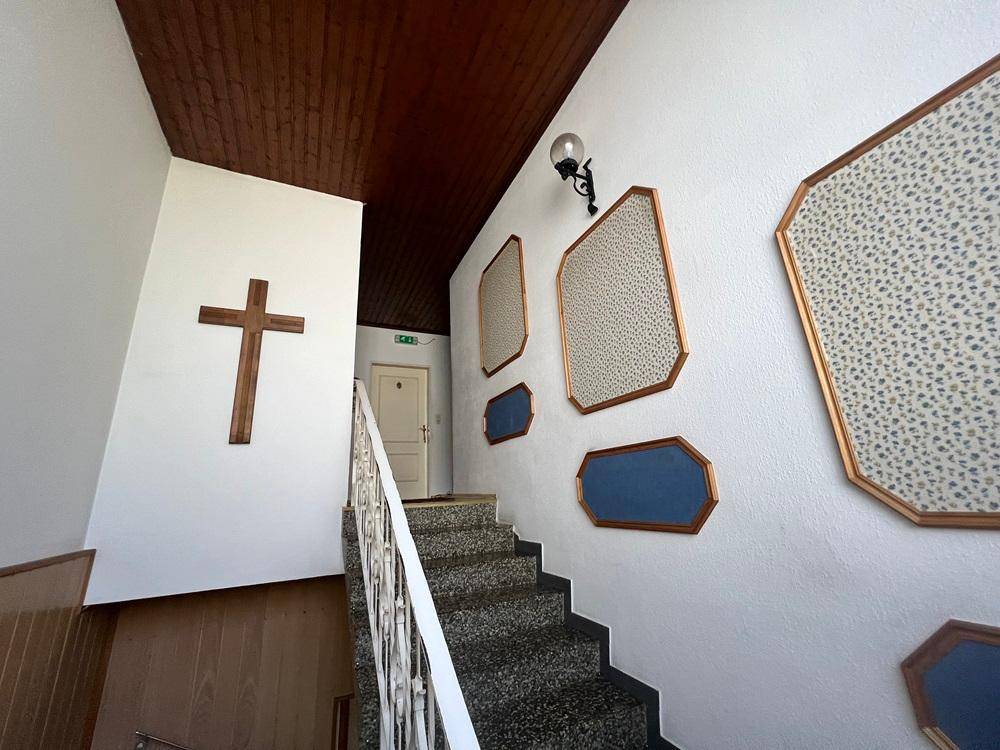 Treppenhaus mit Teppichboden, weiß gestrichenen Wänden und einem Holzkreuz an der Wand.