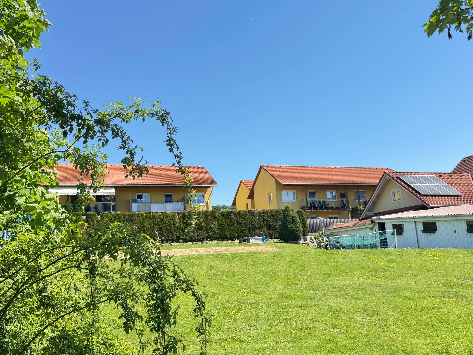 Wohngebäude mit orangefarbenen Dächern und gelben Fassaden, umgeben von Grünflächen und Bäumen.