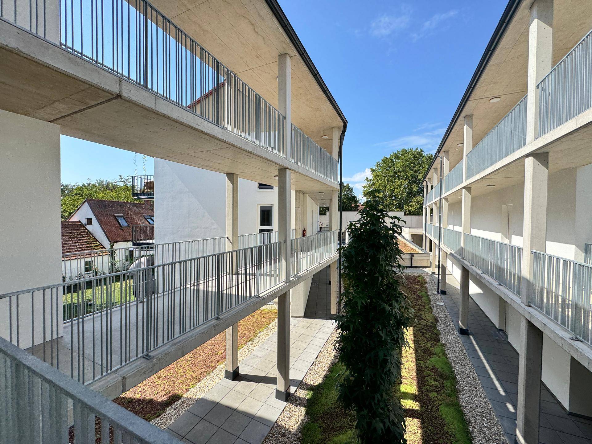 Moderner Innenhof mit klaren Linien, grünen Beeten und Zugang zu den oberen Etagen.