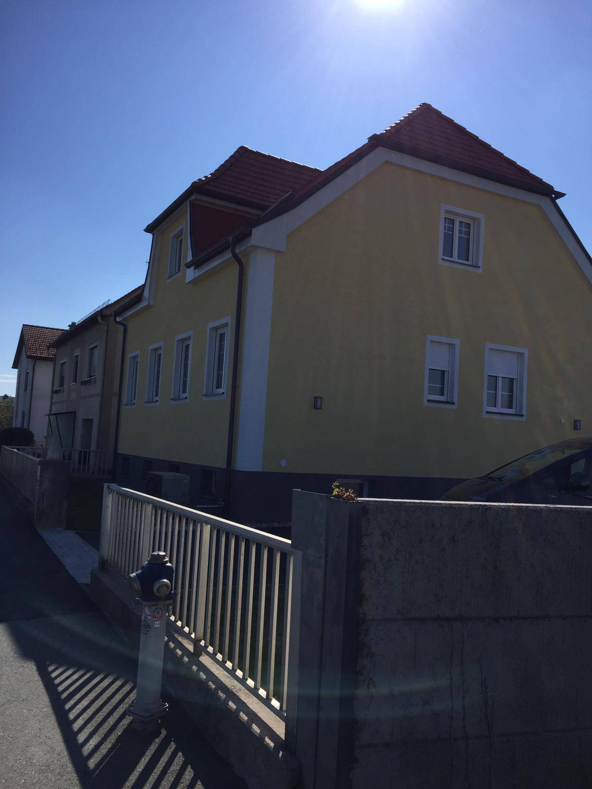 Seitenansicht des frisch renovierten Hauses mit gelber Fassade unter strahlend blauem Himmel.