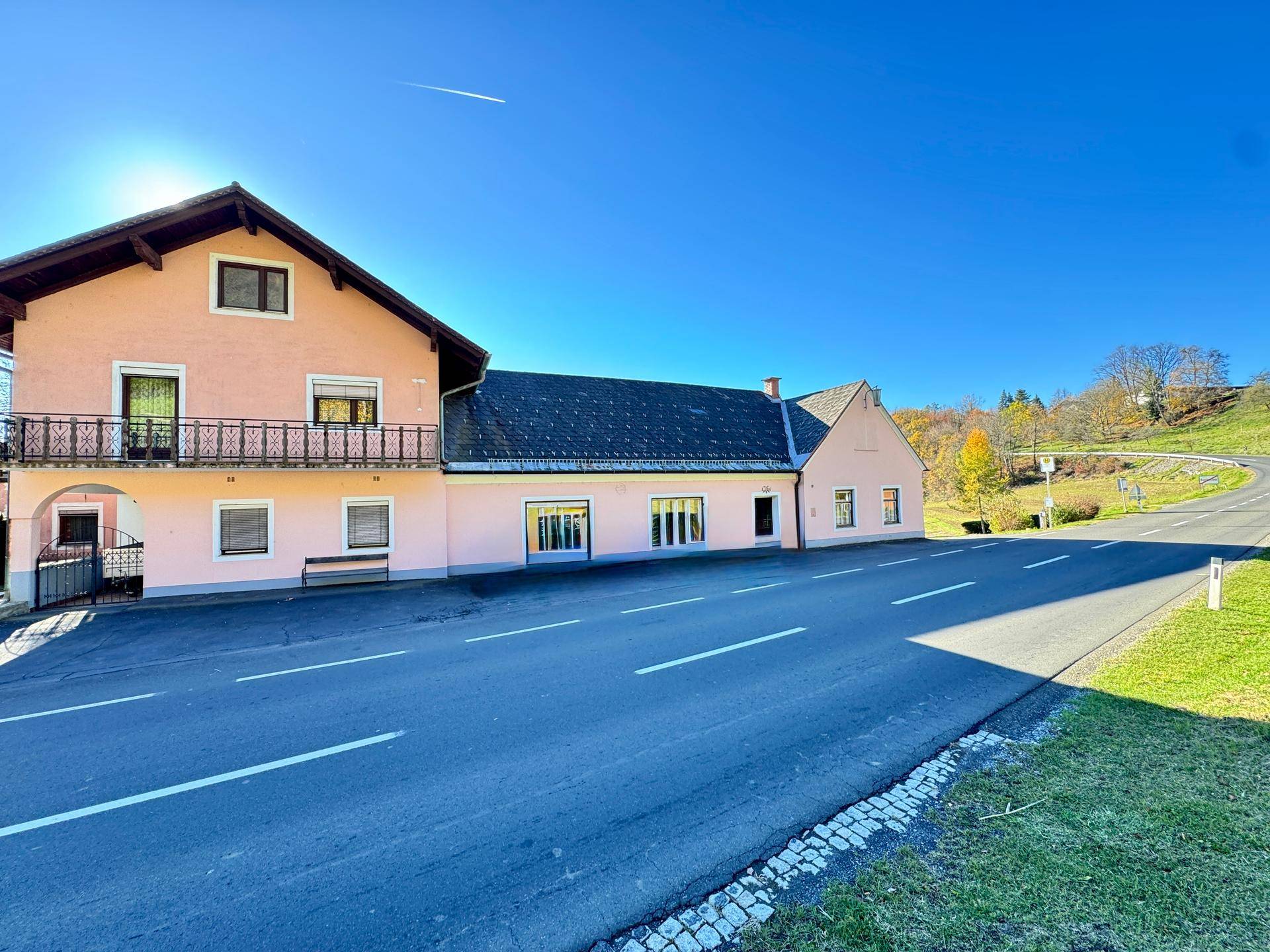 Rosa gestrichenes Gebäude mit Balkon und großen Fenstern, umgeben von einer asphaltierten Straße unter strahlendem Sonnenschein.