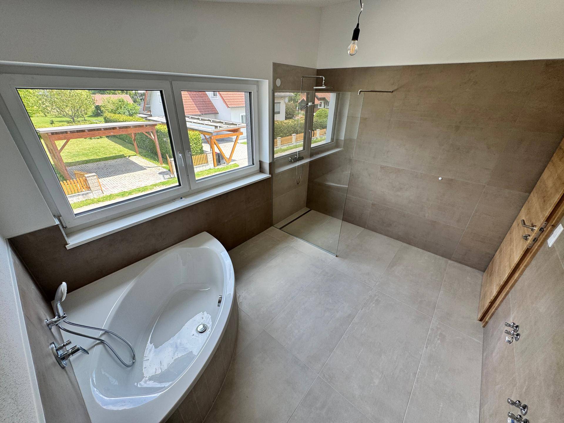 Helles Badezimmer mit Eckbadewanne und Duschbereich, bietet einen Blick ins Grüne.