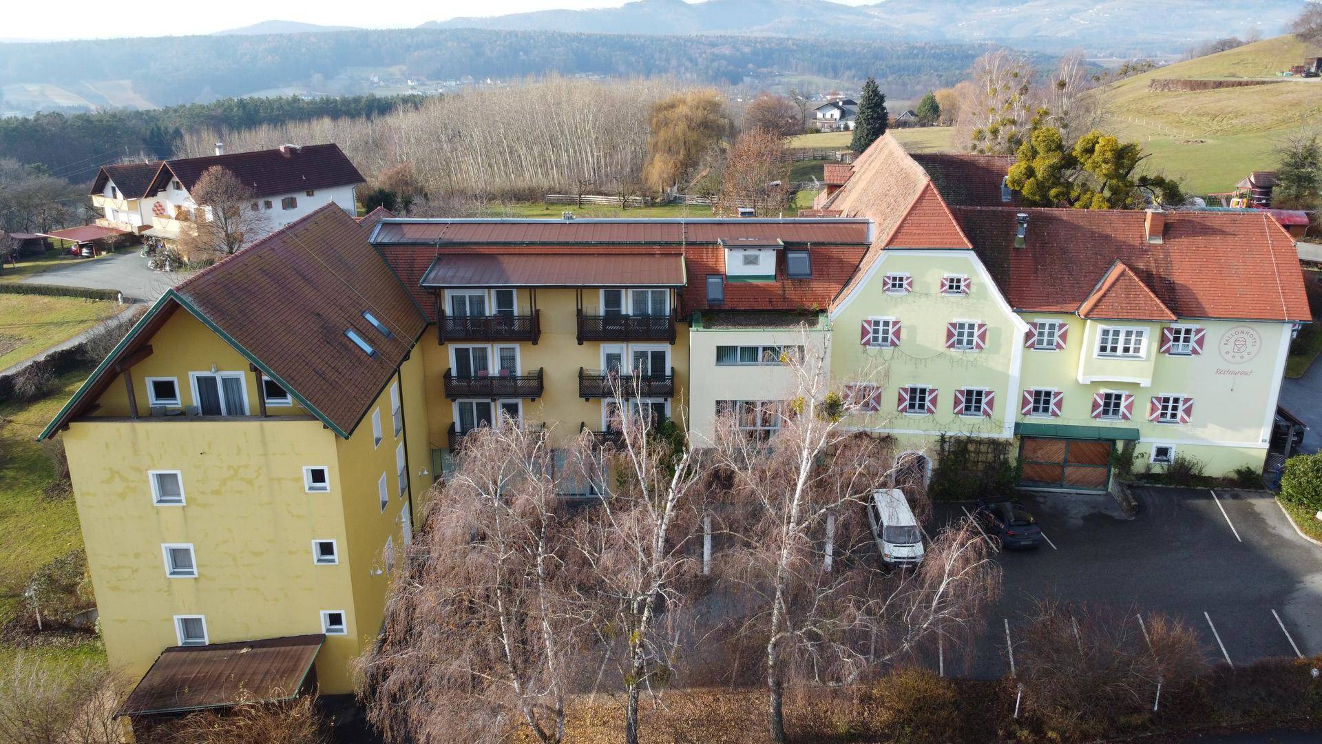 Luftaufnahme des gesamten Gebäudekomplexes mit Parkplatz und weitem Blick auf die Landschaft und Berge.