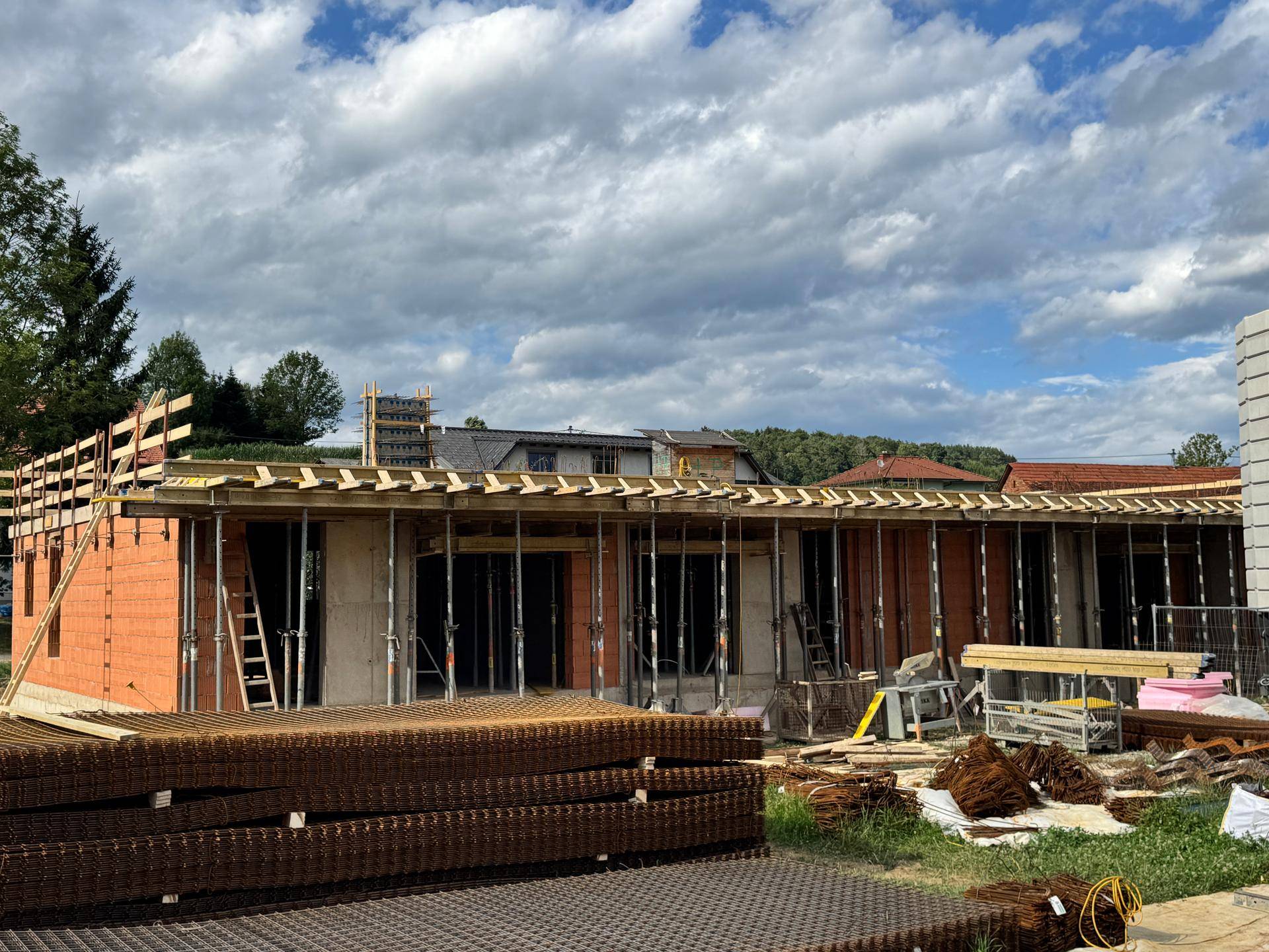 Rohbau eines Gebäudes mit Ziegelwänden und Schalung für die Deckenkonstruktion unter bewölktem Himmel.