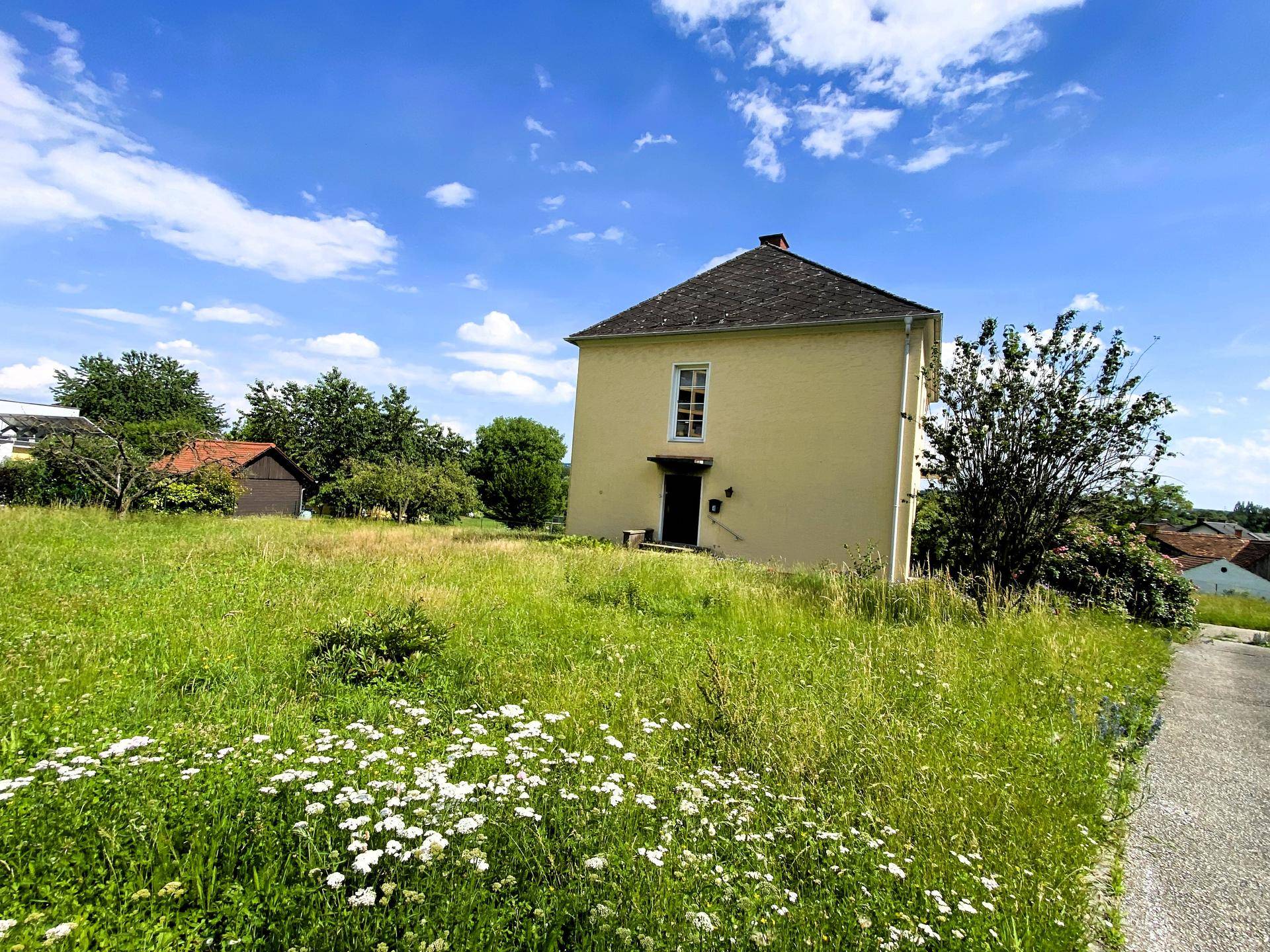 Klassisches gelbes Wohnhaus mit Satteldach und großer Wiese im sonnigen Vordergrund.