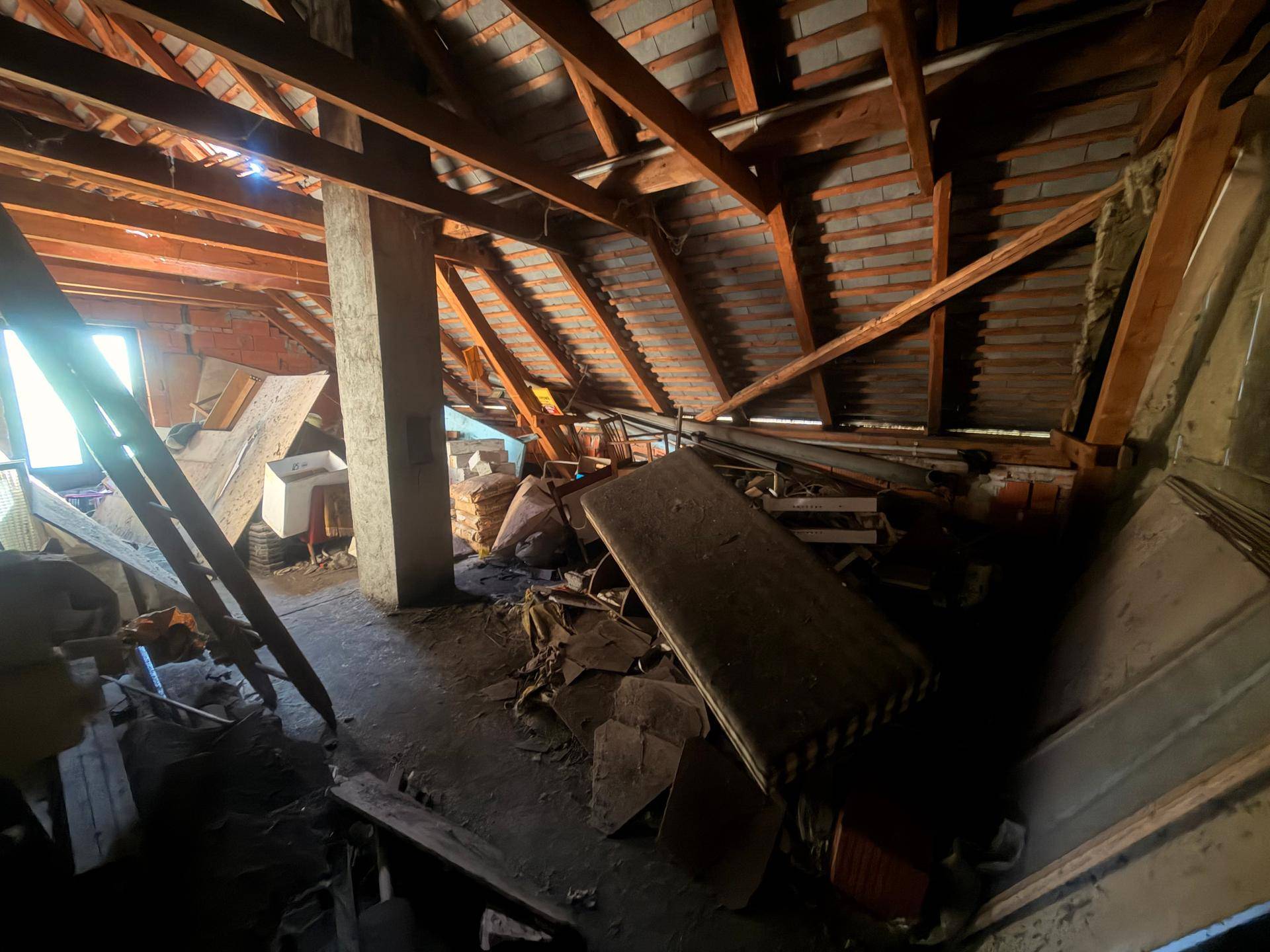 Unausgebauter Dachboden mit sichtbaren Holzbalken und gelagerten Materialien.