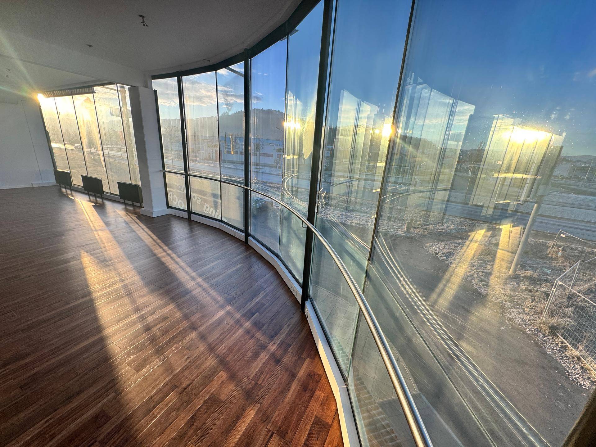 Gebogene Fensterfront mit Blick auf die Umgebung, die viel Sonnenlicht in den Raum lässt.