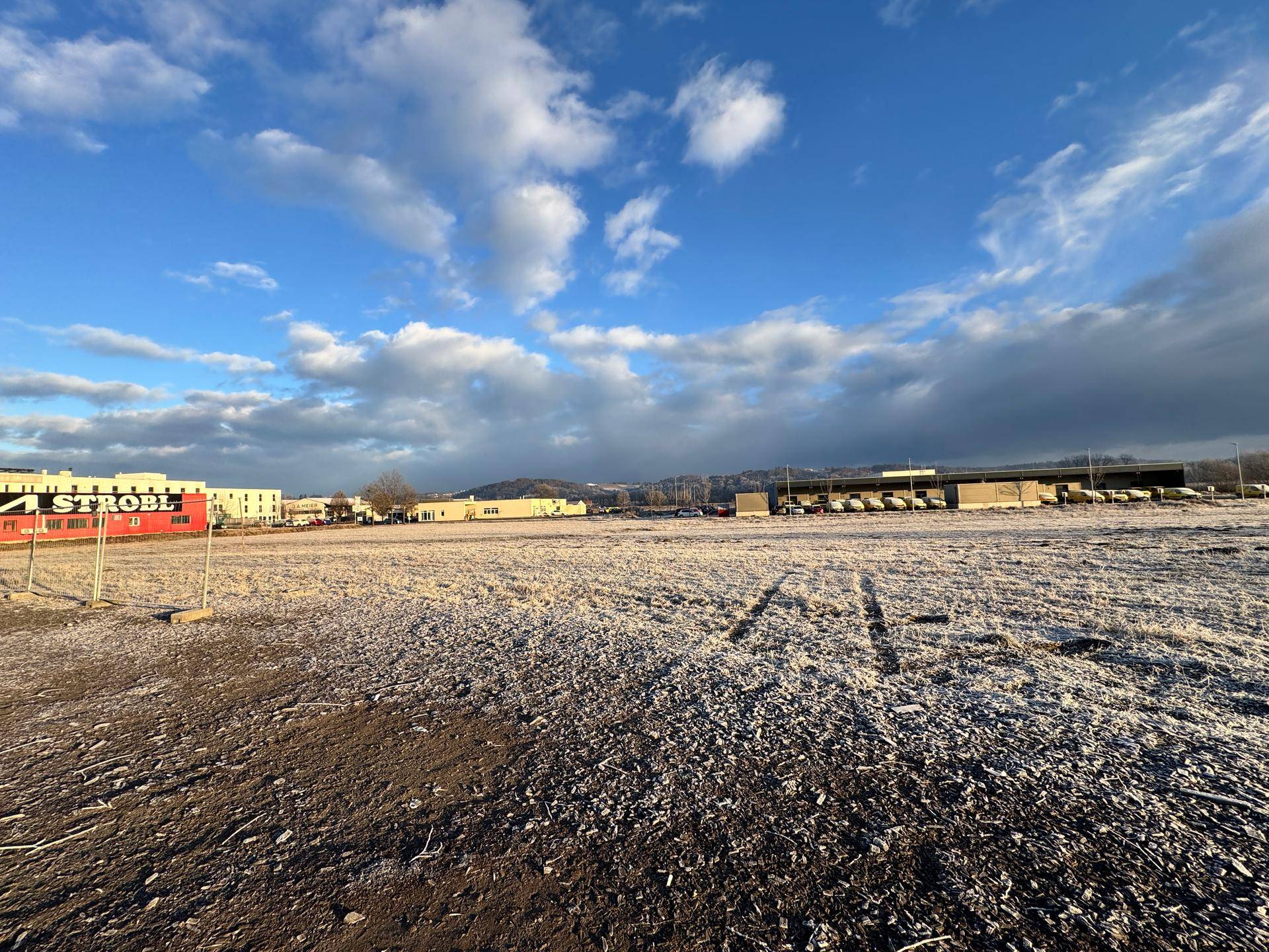 Weitläufiges, frostbedecktes Feld mit Gewerbegebäuden und dem 'STROBL'-Gebäude im Vordergrund unter blauem Himmel.