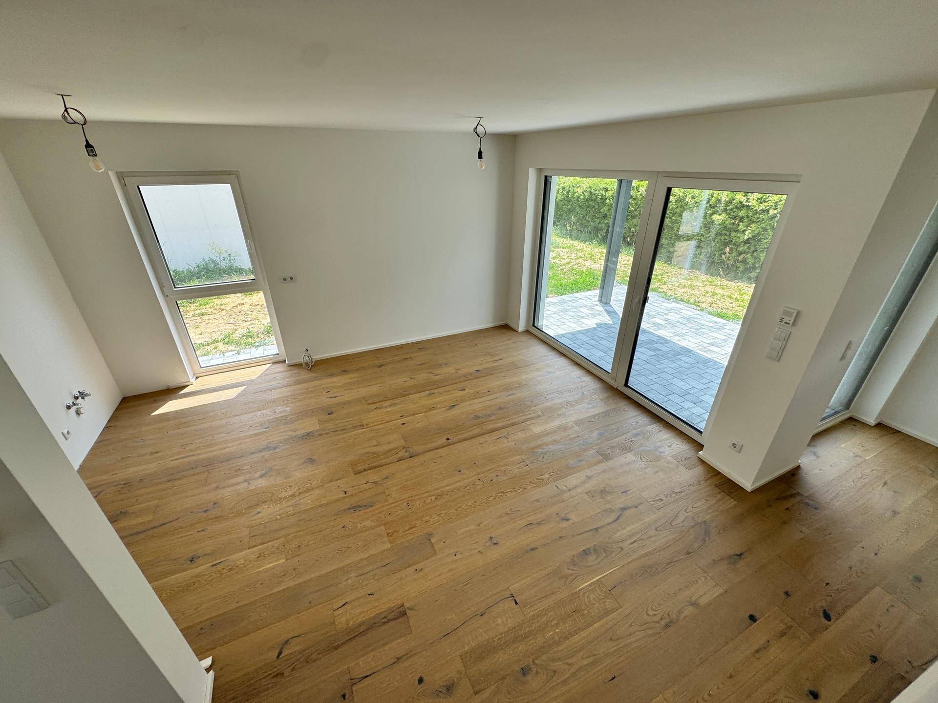 Heller, leerer Raum mit Holzboden und großem Schiebefenster zur Terrasse.
