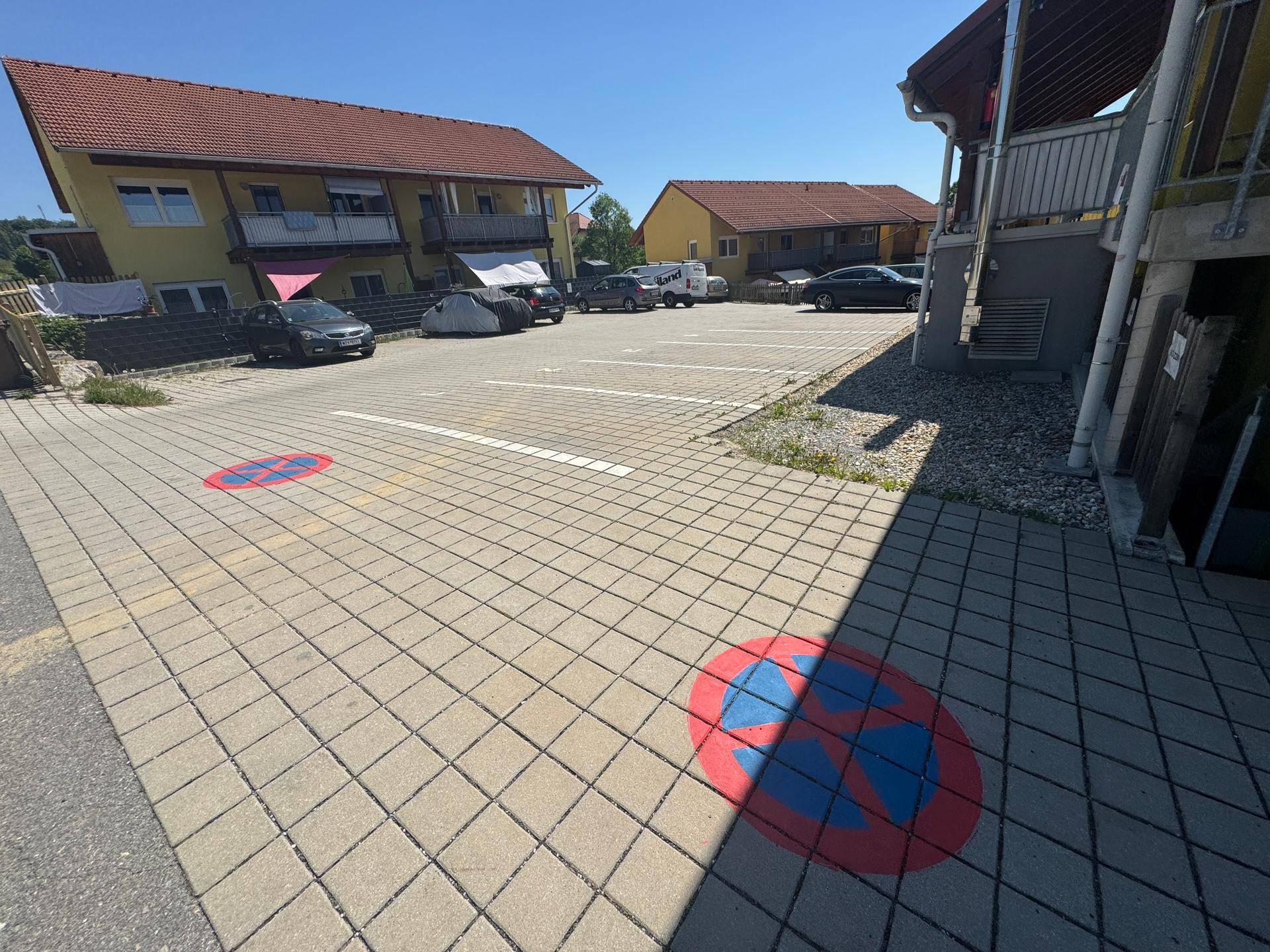 Geräumiger Parkplatz mit Markierungen vor gelben Wohngebäuden unter blauem Himmel.