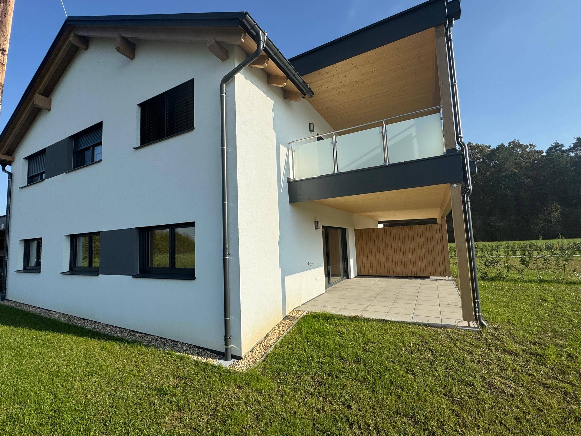 Moderne Doppelhaushälfte mit Balkon und Terrasse, umgeben von viel Grün.