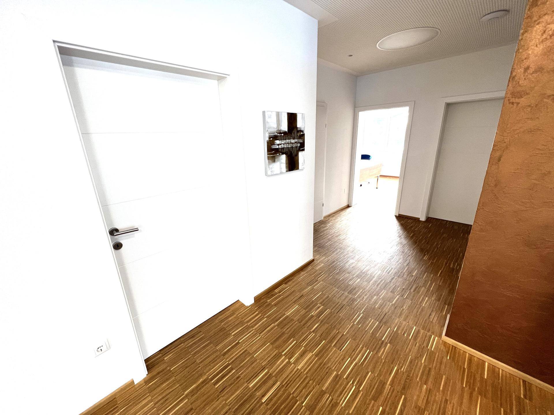 Heller Flur mit Holzboden und modernen weißen Türen, der zu weiteren Räumen führt.