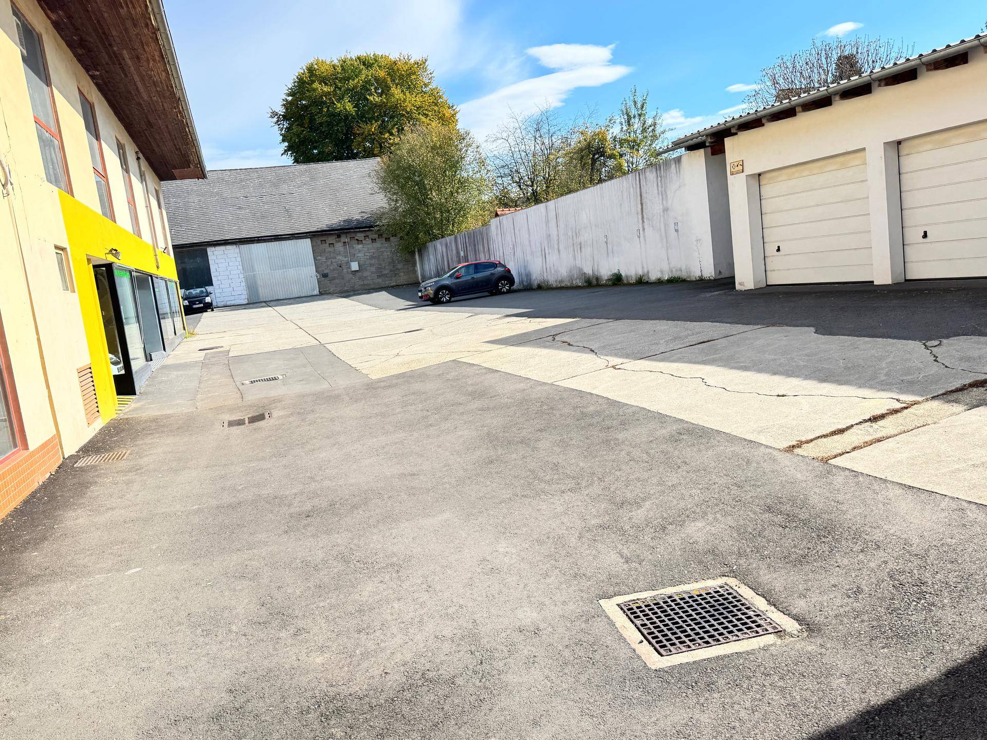 Großer asphaltierter Parkplatz mit Garagen und einem angrenzenden Gebäude, bietet ausreichend Stellflächen.