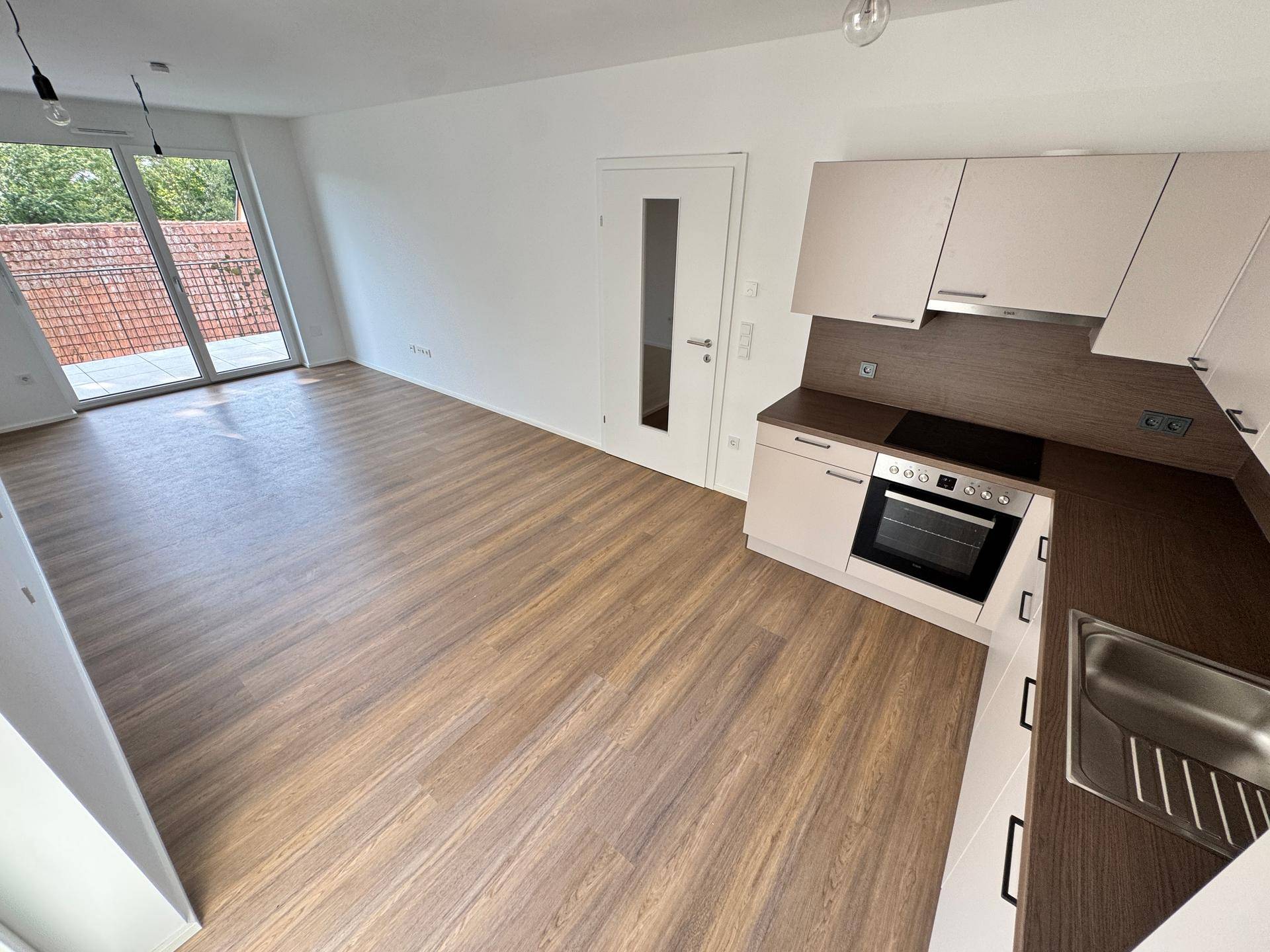 Offener Wohnbereich mit Laminatboden, Zugang zur Terrasse und integrierter Küchenzeile.