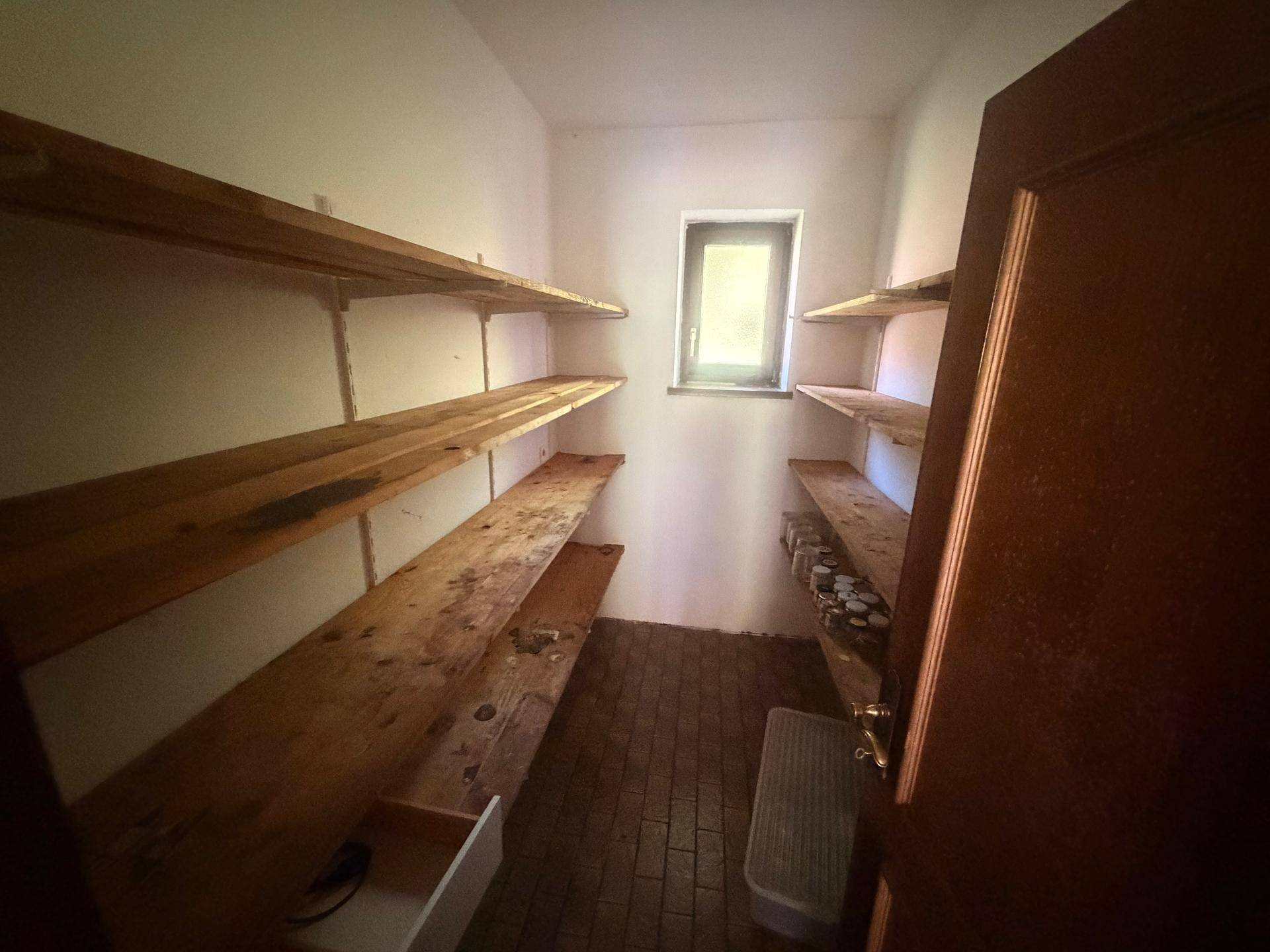 Praktischer Abstellraum mit einfachen Holzregalen und einem kleinen Fenster.