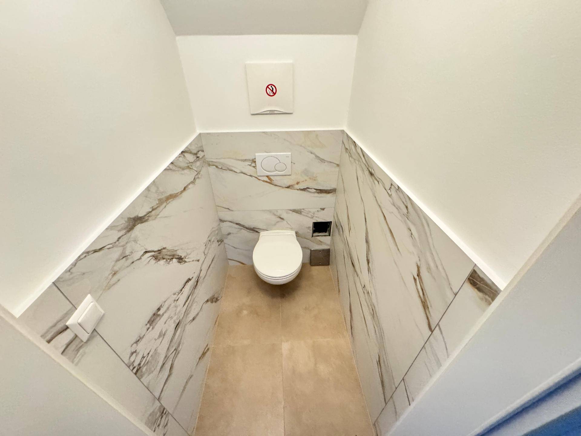 Modernes Gäste-WC mit wandhängender Toilette und eleganten Marmoroptik-Fliesen.
