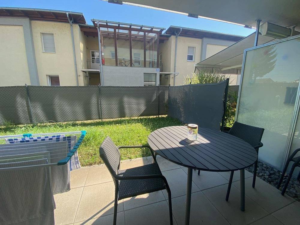 Sonniger Terrassenbereich mit Gartentisch, Stühlen und angrenzender Rasenfläche.